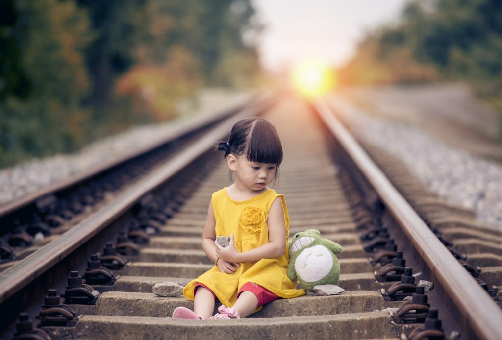 petite fille assise sur une ligne de chemin de fer avec son doudou